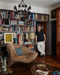 a man standing in front of a bookshelf filled with lots of books and furniture