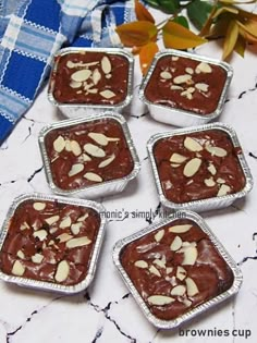 four tins filled with brownies and almonds on top of a white table