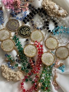 many different colored beads and necklaces on a white cloth with some gold charms attached to them