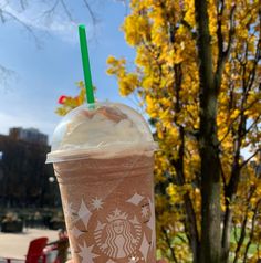 a person holding up a starbucks drink in front of a tree