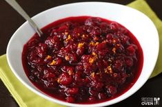 a white bowl filled with cranberry sauce on top of a yellow napkin next to a spoon