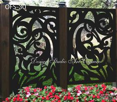 an intricate iron gate with red flowers in the foreground and green grass behind it