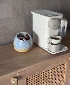 a coffee maker sitting on top of a wooden table next to a bowl with two cups in it