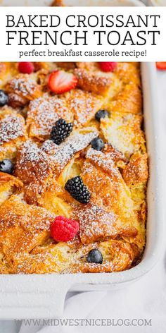 baked french toast in a white casserole dish with berries and powdered sugar