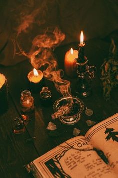 an open book sitting on top of a wooden table next to candles and other items