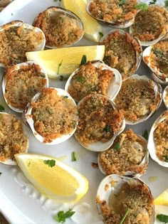 a white plate topped with lots of clams and lemon wedges