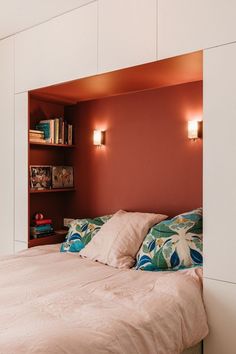 a bed sitting under two lights next to a book shelf in a room with red walls