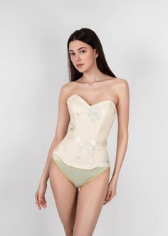 Sunlight Corset is a combination of sophistication and sunny light mood. This corset has a natural push-up effect due to the special arrangement of the bone layout and design. The corset is able to reduce the waist and hips, creating the perfect hourglass silhouette that makes you more feminine. The corset is made of high-quality French satin and transparent net hand-embroidered with sky blue and golden dandelions. It also has transparent paillettes (recycled plastic) imitating the morning dew. Fitted Bodice Underwire Corset With Boning, Shapewear Corset With Underwire And Medium Bust Support, Elegant Shapewear With Sweetheart Neckline, Underbust Shapewear Corset With Lined Body, Beige Sleeveless Corset With Built-in Bra, Fitted Underwire Corset With Lined Body, Strapless Boned Bodice Corset Belt For Summer, Shaping Corset With Built-in Bra And Underwire, Elegant Underbust Lined Body Shapewear