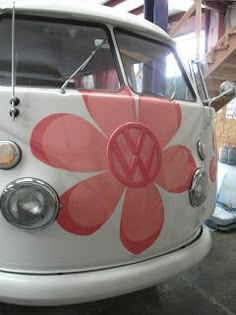 an old vw bus painted in pink and white with a flower on the front