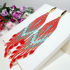 a pair of red and blue beaded earrings sitting on top of a white box