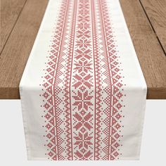 an embroidered table runner with red and white designs on the border, sitting on a wooden surface