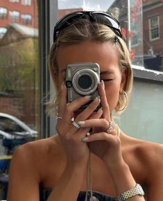 a woman taking a selfie with her camera in front of a window and wearing sunglasses