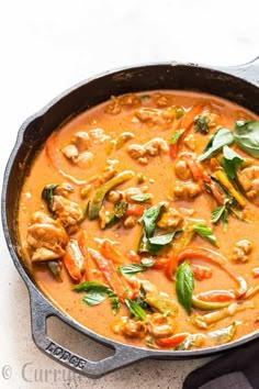 a skillet filled with chicken and vegetables on top of a white counter next to a spoon