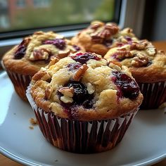 several muffins are sitting on a white plate with blueberries and walnuts