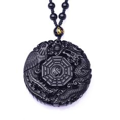 This round obsidian pendant design has a complex pattern carved into this natural stone piece. A dragon and phoenix circle around the ancient yin yang symbol. The Yin Yang symbol is a long known symbol of balance. Together with the phoenix and dragon, this entire pendant is a symbol of matrimonial bliss in Feng Shui. These majestic creatures are intricately crafted onto the pendant which measures 50 x 10 mm. This Innovato Design piece also comes with a long macrame rope necklace adorned with obsidian beads.  Product Highlights    Made with natural obsidian stone  Complex Feng Shui Symbolism Pendant  Macrame Beaded Rope Necklace Symbolic Black Round Jewelry, Traditional Round Jewelry With Dragon Design, Black Amulet Necklace With Coin Pendant, Obsidian Amulet Pendant Necklace, Obsidian Pendant Amulet Necklace, Black Spiritual Jewelry With Coin Pendant, Black Spiritual Necklace With Coin Pendant, Black Coin Pendant Jewelry, Spiritual Black Coin Pendant Jewelry