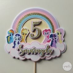 a cake topper with the number five in front of a rainbow and ponies