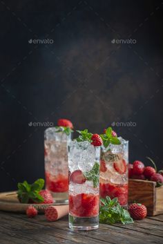 two glasses filled with ice and strawberries on top of a wooden table - stock photo - images