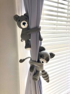 two stuffed bears hanging from the side of a window curtain in front of white blinds