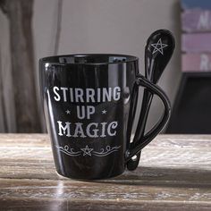 a black coffee cup with the words stirring up magic written on it and a spoon