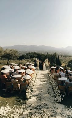 an outdoor ceremony with tables and umbrellas set up on the side of a path