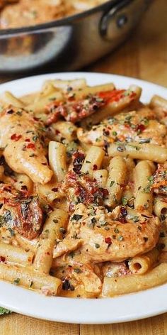 a white plate topped with pasta and meat covered in sauce on top of a wooden table