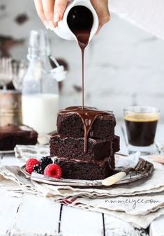 someone is pouring chocolate sauce on a piece of cake with berries and raspberries