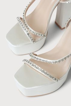 Lulus Exclusive! Feel like you're stepping out onto the stage in the Lulus Sinia Ivory Satin Rhinestone Platform High Heel Sandals! Sleek satin shapes these statement-making heels that have a square toe footbed atop a 1.75"" toe platform. Clear rhinestones, in silver settings, adorn the toe strap, vamp strap, and the matching wrapping ankle strap that secures with a silver buckle. 5. 5" wrapped black heel. Cushioned insole. Felted rubber sole has nonskid markings. Man made materials. Imported. L White Satin Evening Sandals, Glamorous Platform Sandals For Wedding, Glamorous Satin Heels For Prom, Satin Heels With Rhinestones For Prom, Glamorous Embellished Satin Heels, Embellished Synthetic Sandals For Wedding, Glamorous Synthetic Sandals For Wedding, Satin Platform Heels For Party, Rhinestone Synthetic Heels For Wedding