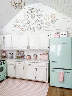 a kitchen with white cabinets and pink gingham rugs on the wooden floor