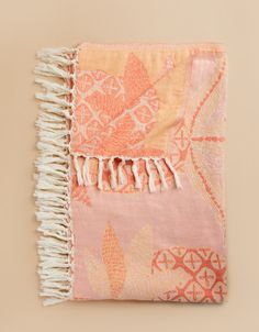 an orange and pink blanket with fringes on top of it, against a beige background