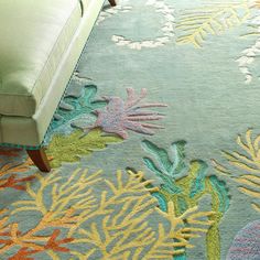 a blue couch sitting next to a rug covered in colorful corals and seaweed