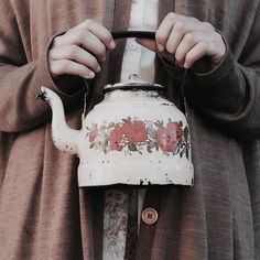 a woman holding a tea pot with flowers painted on it