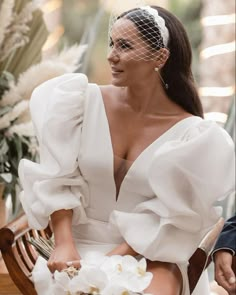 a woman sitting on top of a wooden bench wearing a white dress and headpiece