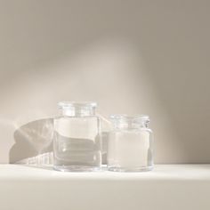 two glass jars filled with white liquid sitting on top of a table