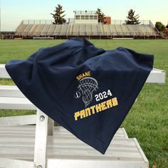 a blanket sitting on top of a white bench in front of a field with an empty bleachers