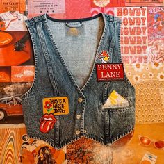 Available in a dark blue wash, this patched retro vest gets finished off with a button-down front closure, gingham stitched pockets, and a cropped length. -Cotton -Patches will vary and pocket color too! -Penny Lane patch will appear in all of them. Jean Vest With Patches, Nostalgia Summer, Patch Vest, Retro Vest, Button Vest, Vest And Tie, Summer 2025, Jean Vest, Penny Lane