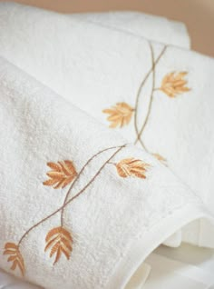 two white towels with embroidered leaves on them