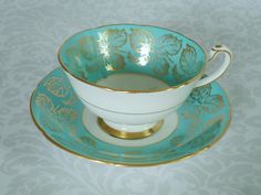 a tea cup and saucer sitting on top of a plate with gold trimmings