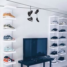 a television sitting on top of a black table in front of a wall filled with shoes