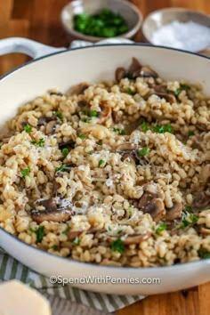 mushroom riso with parsley in a white bowl on a wooden table next to spoons