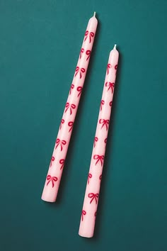 two pink candles with red bows on them sitting next to each other in front of a green background