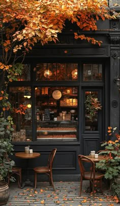 two tables and chairs in front of a store with autumn leaves on the outside windows