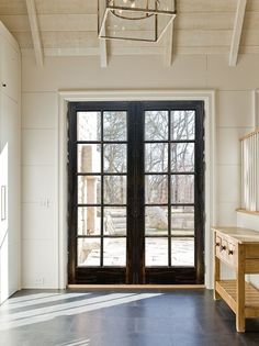 an empty room with two large windows and a bench in front of the door that is open