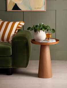 a living room with a green couch and white vase on the table next to it