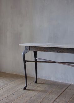 an old table sitting on top of a wooden floor next to a wall with a plant growing out of it