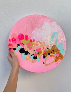 a person holding up a pink paper plate with colorful paint on it and the word love painted on it