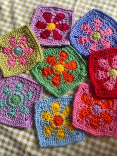 six crocheted squares are arranged on a checkered tablecloth, with flowers in the center