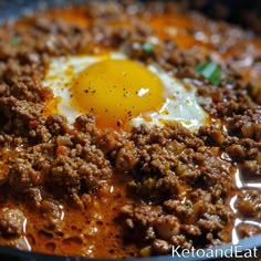 an egg is sitting on top of some meat in a skillet with sauce and seasoning