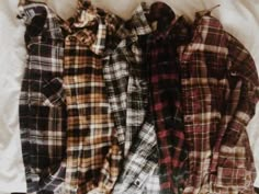 three flannel shirts laid out on top of a white sheet with one laying down