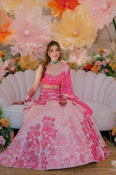 a woman in a pink dress sitting on a white couch with large paper flowers behind her