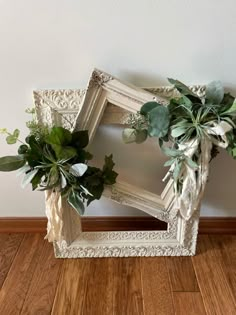 a white frame with flowers and greenery on the floor in front of a wall